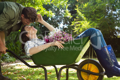 Couple looking face to face while pushing wheelbarrow in garden