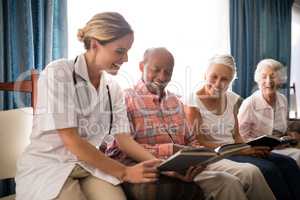 Smiling female doctor reading book to senior people sitting on furniture against window