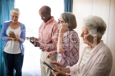 Seniors using mobile phone while standing against window