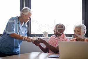 Smiling healthcare worker serving coffee to senior man sitting by friend