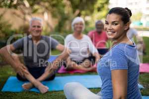 Smiling trainer sitting with senior people while exercising