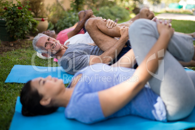 Smiling senior man and friends exercising while lying down by trainer