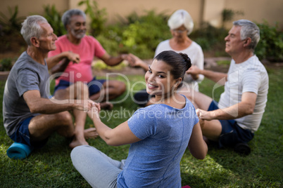 Happy trainer holding hands with senior people while meditating