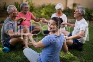 Happy trainer holding hands with senior people while meditating