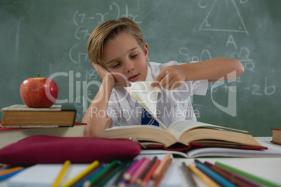 Schoolboy reading book in classroom