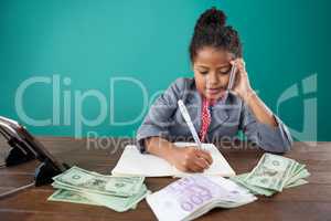 Businesswoman using phone while writing on book by paper currency