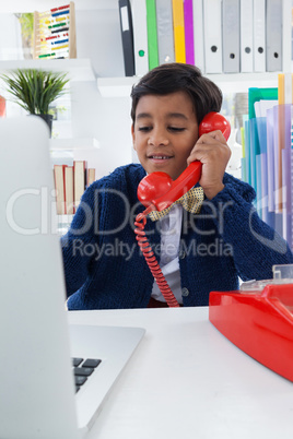 Smiling businessman using laptop while talking on landline phone