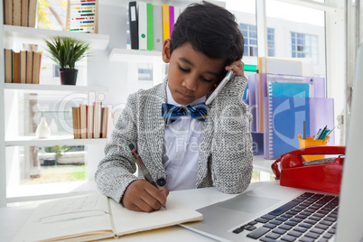 Businessman writing on book while talking on smartphone