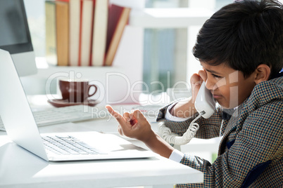 Businessman talking through telephone while pointing on laptop at desk