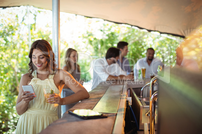 Smiling woman using mobile phone while having a glass of beer