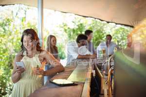 Smiling woman using mobile phone while having a glass of beer