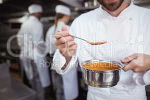 Chef checking food from spoon in kitchen at restaurant