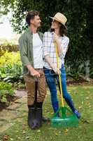 Happy couple standing with gardening rake and shovel in garden