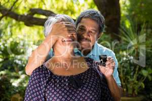 Senior man covering woman eyes while gifting her ring