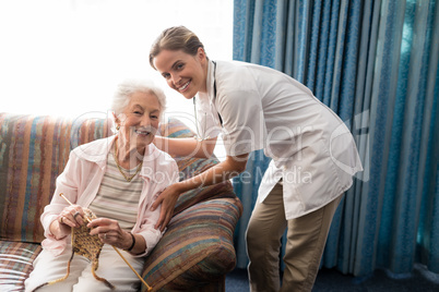 Portrait of smiling senior woman holding knit with female doctor against window