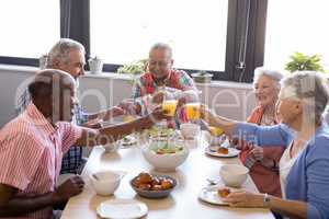 Happy senior people toasting juice glasses at table