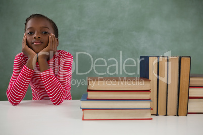 Schoolgirl sitting beside books stack against chalkboard