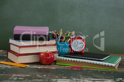 Stack of books with alarm clock, apple and pen holder