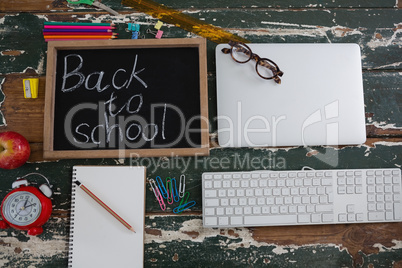Back to school text written on chalkboard with various stationery, apple and electronics