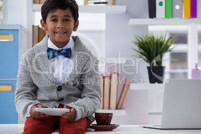 Portrait of happy businessman holding mobile phone while sitting on desk