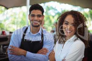 Portrait of smiling waiter and waitress standing with arms crossed at counter