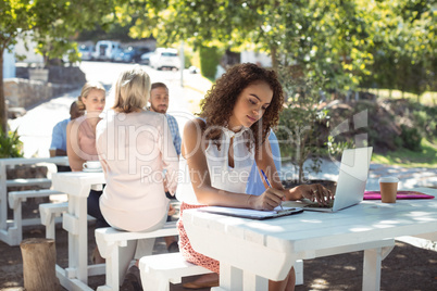 Beautiful woman writing on clipboard while using laptop