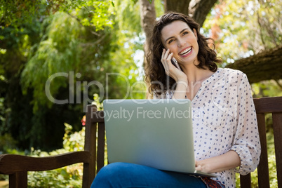 Woman talking on mobile phone while using laptop