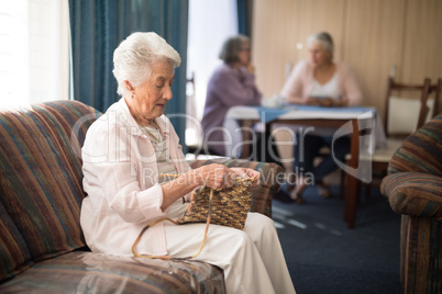 Side view of senior woman knitting while sitting on sofa