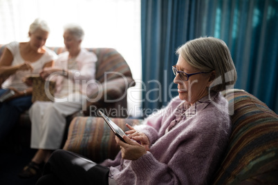 Senior woman using digital tablet while sitting on armchair