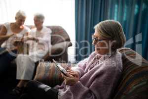 Senior woman using digital tablet while sitting on armchair