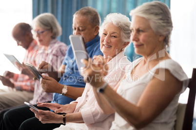 Senior people sitting on chairs while using digital tablets