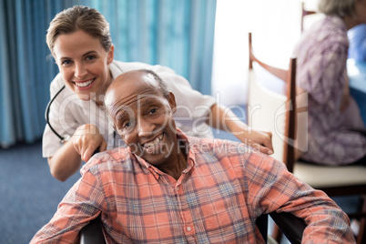 Portrait of cheerful female doctor standing with disabled senior man on wheelchair