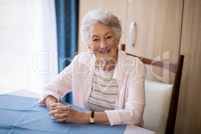 Portrait of smiling senior woman sitting with hands clasped