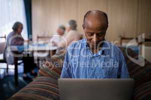 Smiling senior man using laptop while sitting on sofa