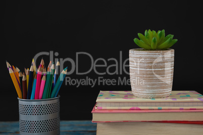 Pot plant, color pencils and book stack on wooden table