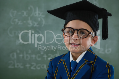 Schoolboy in mortar board standing against chalkboard