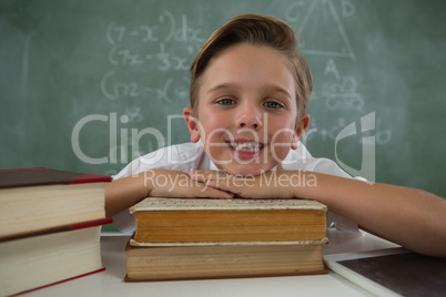 Schoolboy relaxing on books in classroom