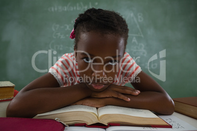 Schoolgirl relaxing on open book in classroom