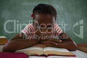 Schoolgirl relaxing on open book in classroom