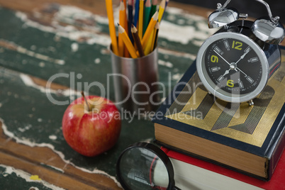 Alarm on stack of books with pen holder, apple, and magnifying glass