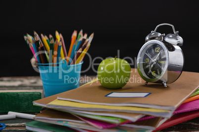 Alarm clock and apple on stack of books with pen holder