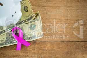High angle view of paper currency and pink Breast Cancer Awareness ribbon by piggybank on wooden tab