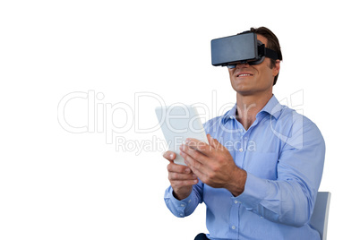Smiling businessman with tablet sitting on chair while using vr glasses
