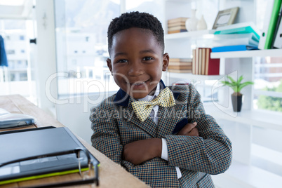 Portrait of smiling boy imitating as businessman sitting with arms crossed
