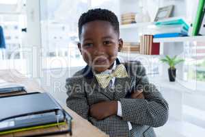 Portrait of smiling boy imitating as businessman sitting with arms crossed