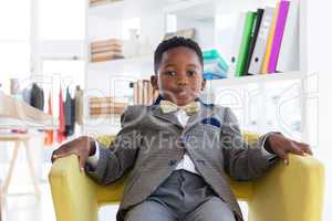 Portrait of boy imitating as businessman sitting on armchair
