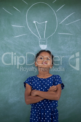 Girl with arms crossed standing by bulb drawing on wall