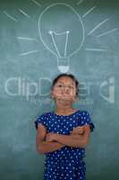 Girl with arms crossed standing by bulb drawing on wall