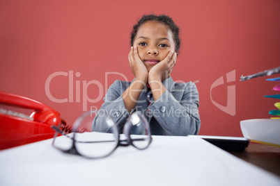 Girl imitating as businesswoman sitting with hand on chin