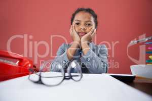 Girl imitating as businesswoman sitting with hand on chin